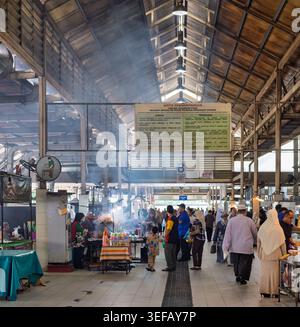 Bandar Seri Begawan, Brunei - 26. Februar 2025: Gadong Night Market mit Händlern, die kochen, Rauch aufsteigen und Menschen, die an den Imbissständen unter dem Dach des Marktes vorbeischauen Stockfoto