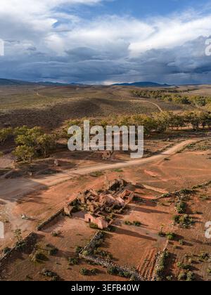 Aus der Vogelperspektive auf die historischen Ruinen der Kanyaka Station, umgeben von roter Erde, Feldwegen und karger Vegetation unter einem dramatischen bewölkten Himmel in Flinders Stockfoto