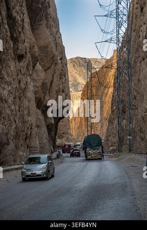 Der Verkehr bewegt sich durch eine enge Schlucht mit hoch aufragenden Felswänden und Stromleitungen in Afghanistans rauer Landschaft Stockfoto