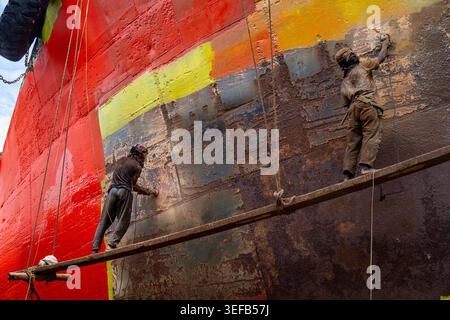Männer reparieren ein Boot in einer Schiffswrack-Werft in Dhaka, Bangladesch, während sie an der rostfreien Oberfläche arbeiten und sich für die Lackierung vorbereiten Stockfoto