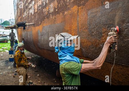 Männer reparieren ein Boot in der Schiffswrack-Werft, konzentrieren sich auf den Rumpf und verwenden Werkzeuge, um Rost und alte Farbe auf einer Baustelle in Bangladesch zu entfernen Stockfoto