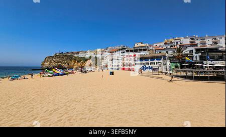 Besucher genießen einen sonnigen Tag am Strand mit farbenfrohen Booten in Carvoeiro Algarve Portugal Stockfoto