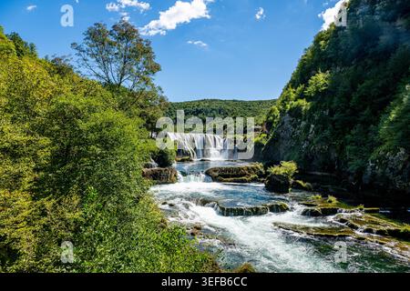 Der Strbacki Buk Wasserfall im Una Nationalpark fließt an einem sonnigen Tag in Bosnien und Herzegowina über Felsen und kaskadiert durch Bäume Stockfoto