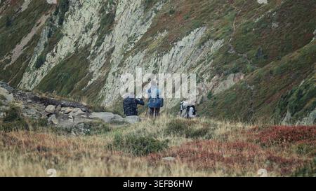 Refuge de Bellachat, Frankreich - 20.09.2025: Eine Gruppe von drei Rucksacktouristen, die durch eine pulsierende Landschaft aus roten und goldenen Alpensträuchern auf einem steilen m wandern Stockfoto