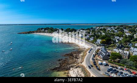Legenese Cove Beach bietet einen Blick auf Wellen, Sand und Häuser entlang der Küste in der Bretagne, Frankreich an einem sonnigen Tag Stockfoto