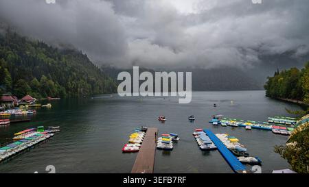 Bootssteg auf dem Ritsa See mit Booten und bewölktem Himmel, Ritsa Relict Nationalpark, in Russland an einem bewölkten Tag Stockfoto