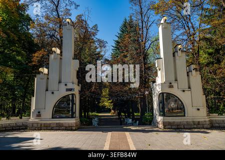Historischer Eingang zu einem Park in Wladikawkaz mit hohen Säulen und Bäumen im Hintergrund an einem hellen Tag Stockfoto