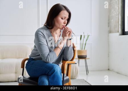 Depressive, besorgte reife Frau, die auf einem Stuhl sitzt, zu Hause Stockfoto