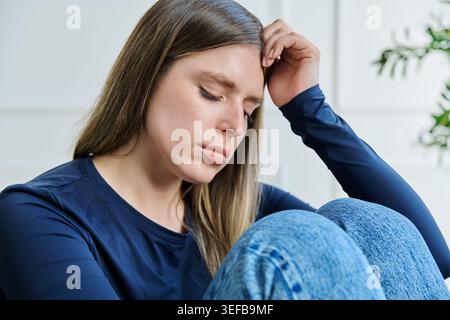 Unglückliche, verärgerte junge Frau, die zu Hause auf einem Stuhl sitzt Stockfoto