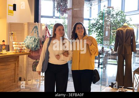 Zwei Freundinnen, die Arm in Arm gehen, gehen gerne Kleidung in einer Boutique einkaufen Stockfoto