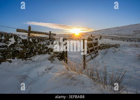 Sonnenaufgang durchbricht schneebedeckte Landschaft mit Tor und Steinmauer in Wildboarclough, Peak District, Cheshire Stockfoto