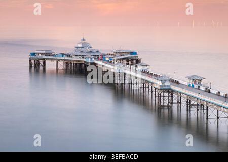 Llandudno Pier und die Fernwindturbinen des Gwynt y Mor Offshore Wind Farm at Sunset, Llandudno, Conwy County Borough, North Wales, Großbritannien Stockfoto