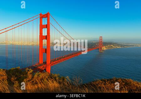 Die Golden Gate Bridge überspannt das Wasser in San Francisco bei Sonnenuntergang mit der Skyline der Stadt in der Ferne Stockfoto