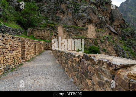 Erkunden Sie Inka-Ruinen und Steinwege an der archäologischen Stätte Ollantaytambo in Peru, umgeben von Bergen und Grün Stockfoto