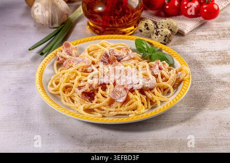 Appetitliches Spaghetti Carbonara Gericht, reichhaltige cremige Sauce, herzhaften Speck, frisches Basilikum. Helle Beleuchtung hebt goldene Nudeln, leuchtendes Grün, rosa Speck hervor Stockfoto