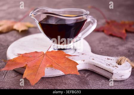Ahornsirup in einem Glas Soße Boot auf grauem Hintergrund. Stockfoto