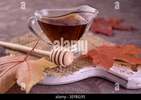 Ahornsirup in einem Glas Soße Boot auf grauem Hintergrund. Stockfoto