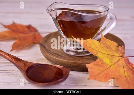 Ahornsirup in einem Glas Soße Boot und Ahornblätter. Stockfoto