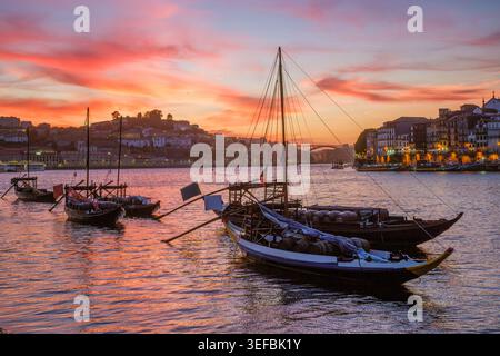 Porto-Rbelo-Boote auf dem Fluss Douro bei Sonnenuntergang in der Nähe von Ribeira, Portugal, mit warmen Dämmerungsfarben, vertäuten Booten und Reflexionen am Wasser, Panoramablick Stockfoto