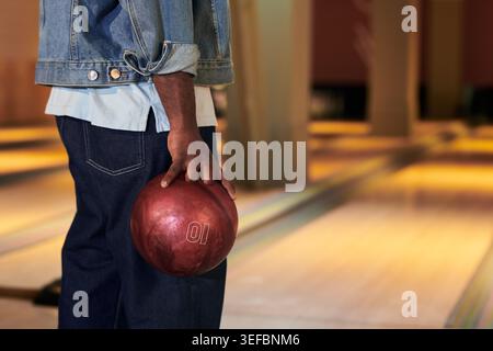 Junger Erwachsener, der Bowlingball neben der Bahn hält und während des Freizeitspiels den Wurf vorbereitet. Bildunterstützung für Freizeitmarketing, Teambindung, Social-Media-Kampagnen Stockfoto
