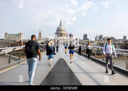 Stadtarbeiter gehen über die Millennium Bridge, während sie in die City of London mit der St Paul's Cathedral in der Ferne, London, England, Großbritannien, pendeln. Stockfoto