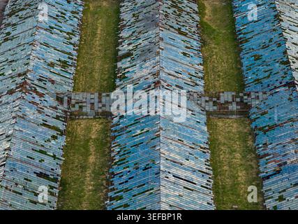 Aus der Vogelperspektive verlassene Gewächshäuser mit gebrochenen blauen Glaspaneelen und grünen Grasreihen im Kreis Vilnius, Litauen. Stockfoto