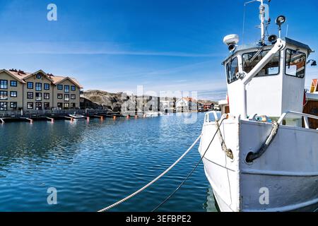 Das Boot ist am Ufer mit einem Seil am Dock verankert. Farbenfrohe Häuser und Gebäude säumen den Hafen in einer kleinen Küstenstadt. Stockfoto