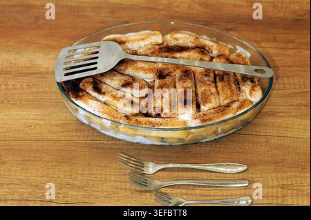 Tiramisu-Dessert mit kaffeeingetränkten Ladyfingers, Sahne und Kakaopulver in einer Glaspfanne auf einem Holztisch, mit Metallspachtel und Thr Stockfoto