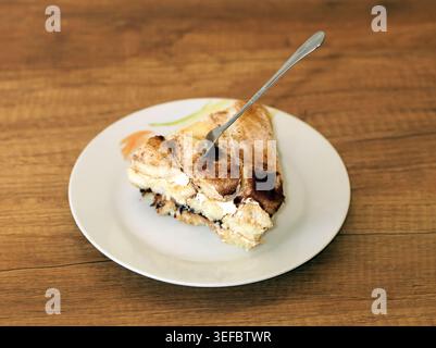 Tiramisu-Scheibe, zubereitet mit Ladyfingers, Kaffee, Mascarponesahne und Kakaopulver auf einer weißen Keramikplatte, mit einer Silbergabel, die in den Th gräbt Stockfoto