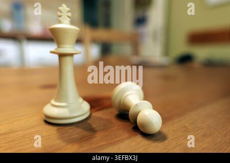 Weißer Schachkönig, der hoch auf einer Holzfläche steht, während ein Schachfiguren daneben liegt und Konzepte von Strategie, Sieg, Niederlage und Wettkampf veranschaulicht Stockfoto