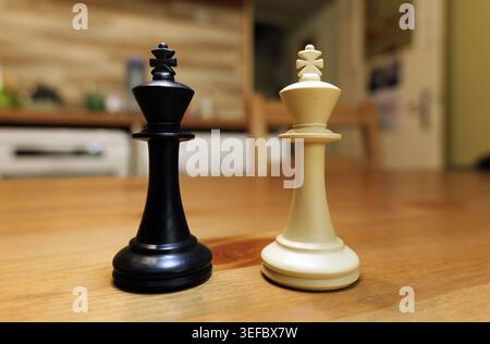 Schachkönige, ein Schwarzer und ein Weißer, stehen auf einem Holztisch, repräsentieren Strategie, Wettbewerb, Entscheidungsfindung und kontrastierende Entscheidungen in einem Ga Stockfoto