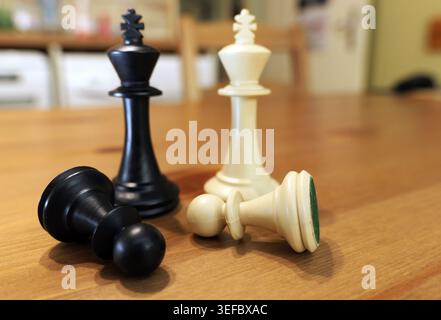 Schachkönige und Schachfiguren auf einem Holztisch, mit zwei gefallenen Schachfiguren, symbolisiert Strategie, Wettbewerb, Sieg, Niederlage, und wichtige Entscheidungen in b Stockfoto