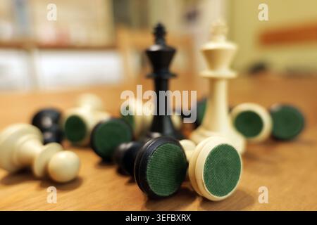 Auf einem Holztisch verstreute Schachfiguren mit den schwarz-weißen Königen, die zwischen den gefallenen Stücken stehen, symbolisieren Konzepte von Strategie und Wettbewerb Stockfoto