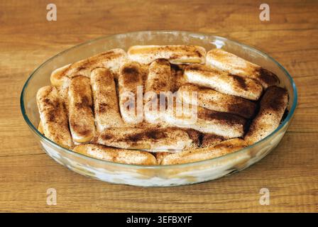 Tiramisu-Dessert mit Schichten Kaffee getränkte Marienfinger und Mascarponcreme, großzügig mit Kakaopulver bestäubt und in einer Glasbackform ruhen Stockfoto