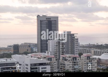 Moderne Gebäude sind in Sonnenuntergang getaucht, Horizont auf dem Meer. Das Stadtbild von Haifa ist vor einem bewölkten Himmel voller Wärme gehalten Stockfoto