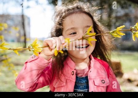 Kaukasisches Mädchen mit blühendem Forsythia-Zweig mit gelben Blüten im sonnigen Parkbereich. Kindheits- und Frühlingsleben. Stockfoto