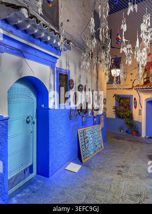 Eine lebendige blaue Tür und eine mit Kunsthandwerk dekorierte Gasse und die ikonischen Indigo-Wände der „Blauen Stadt“ – Chefchaouen, Marokko. August 2025 Stockfoto