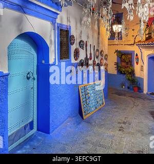 Eine lebendige blaue Tür und eine mit Kunsthandwerk dekorierte Gasse und die ikonischen Indigo-Wände der „Blauen Stadt“ – Chefchaouen, Marokko. August 2025 Stockfoto