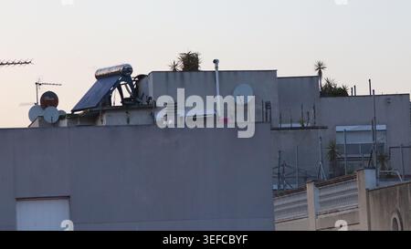 Die Dächer von Wohngebäuden verfügen über ein Solaranlage und Satellitenschüsseln vor einem klaren Himmel in der Dämmerung. Stockfoto