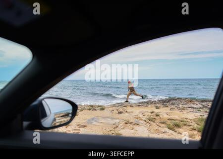 Ein Mann, der an der felsigen Küste entlang läuft und vom Fenster aus betrachtet wird, fängt Freiheit, Abenteuer und den Lebensstil eines Roadtrips an der Küste ein. Stockfoto