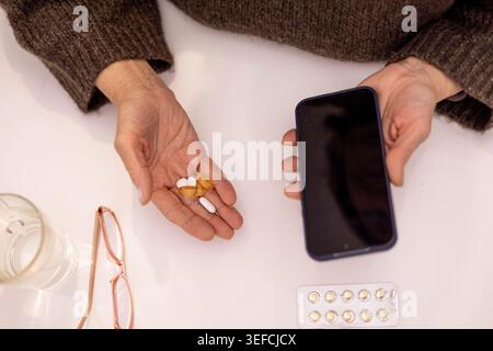 Frauenhände, die Pillen und Smartphone halten, Wellness-Routine. Stockfoto