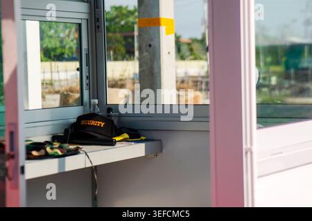 Eine Sicherheitsstation mit uniformiertem Sicherheitshut und Ausrüstung, die auf einem Theken mit Blick auf ein großes Fenster platziert ist, für Überwachung und Stockfoto