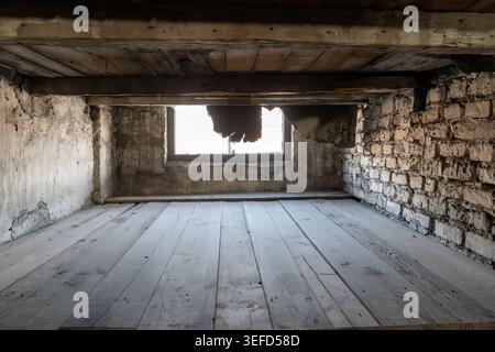 Eine Nahaufnahme fängt den engen Raum einer Gefangenenliege mit Holzdielen ein, die von abgenutzten Ziegeln und abblätternden Betonwänden umgeben sind. Eine teilweise Abdeckung Stockfoto