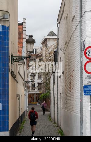Brüssel, Belgien - 2. April 2026: Enge Fußgängerzone verläuft zwischen Ziegelmauern und alten Gebäuden mit Straßenlaterne, Schildern und zwei Personen zu Fuß Stockfoto