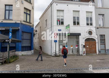 Brüssel, Belgien - 2. April 2026: Fußgänger stehen in der Nähe eines Eckgebäudes aus weißem Backstein mit Holztür, Verkehrsschildern, Fahrrad und schmaler Gasse Stockfoto