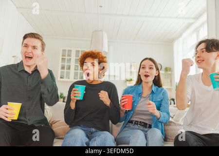 Gruppe von Freunden, die Fußballspiele im fernsehen ansehen. Glückliche Fußballfans feiern den Sieg zu Hause. Freundschaftssport-Entertainment-Konzept. Verschiedene Freunde, die zu Hause Spaß haben Stockfoto
