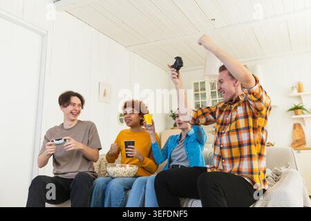 Heimparty. Fröhliche Gruppe von Freunden, die zu Hause Videospiele spielen. Fröhliche Gruppen-Freunde, die gemeinsam viel Spaß haben. Freundschaft Freizeitunterhaltungs-Konzept. Junge beste Freunde genießen das Wochenende Stockfoto