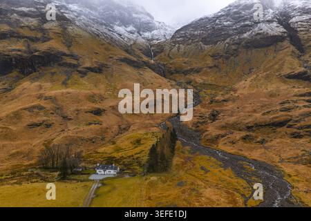 Aus der Vogelperspektive eines weißen Häuschens am Fuße der schneebedeckten Berge in Glencoe, Schottland, Großbritannien. Stockfoto