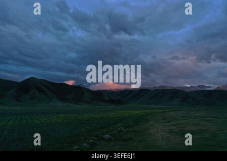 Ein riesiges offenes Feld erstreckt sich über sanfte grüne Hügel unter einem dramatischen Dämmerhimmel, der von dunklen Wolken erfüllt ist, die in sanften Rosa-Tönen in der Nähe der Hor getönt sind Stockfoto