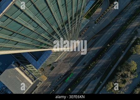 Aus der Vogelperspektive ist ein eleganter Glashochhaus zu sehen, der die Umgebung mit einer breiten Autobahn, die unter dem imposanten Gebäude fließt, dominiert. Stockfoto